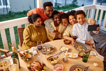 High angle portrait of happy African American family taking selfie photo at house terrace in evening