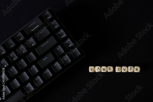 Game over inscription on a black background next to a black gaming keyboard. Concept for eSports. Fatum, gambling addiction and the predetermination of the finale.