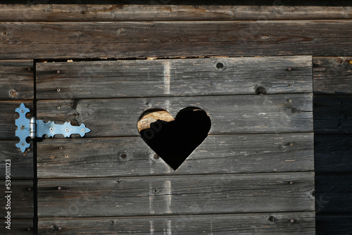 outdoor wooden toilet door fragment with cut heart symbol and metal hinge
