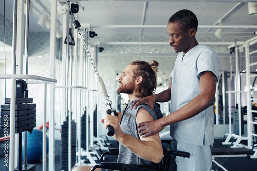 African doctor training patient with disability on exercise equipment during his rehabilitation