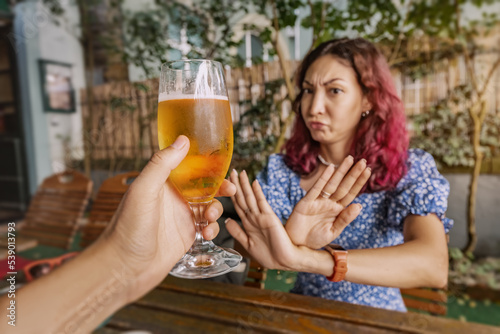 Funny sober woman refuses an extra glass of beer at the pub. Say no and stop to addiction and excessive alcohol consumption. photo