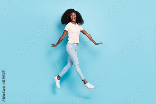 Full size portrait of overjoyed satisfied girl jumping enjoy free time isolated on blue color background
