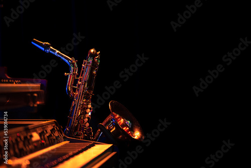 Canvas Print Saxophone in black environment standing behind a piano keyboard