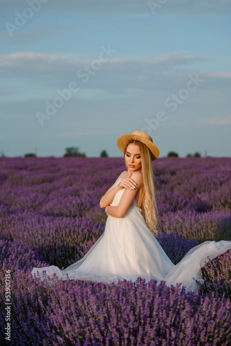 Young beautiful woman in a white dress and a hat is walking in the lavender field.