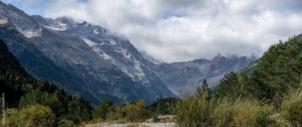 magnificent view of a long glacial forested valley through cloud topped Spanish Pyrenees mountains