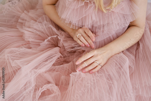 Beautiful female hands on a pink background of a puffy dress. Aesthetics of minimalism. The concept of spa, wedding salons, hand treatments