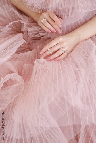 Beautiful female hands on a pink background of a puffy dress. Aesthetics of minimalism. The concept of spa, wedding salons, hand treatments 