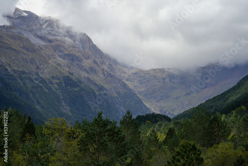 view along a glacial forest lined valley to a massive mountainous amphitheater  cirque  with cloud forming on the mountain tops  
