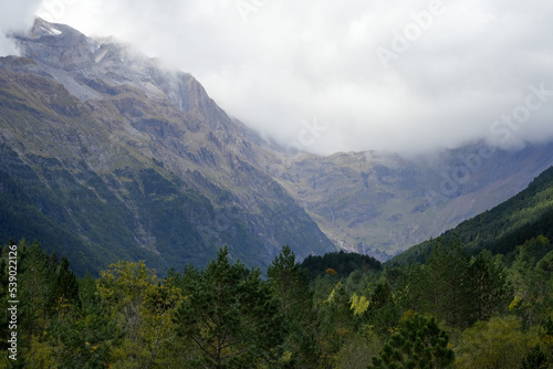 view along a glacial forest lined valley to a massive mountainous amphitheater (cirque) with cloud forming on the mountain tops 