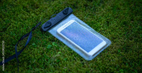 Smartphone in a waterproof case on the green grass. Means to prevent moisture from entering the phone. A plastic case for a smartphone when traveling and on vacation.