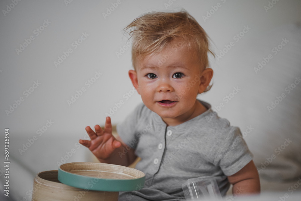 cute happy one year old blond baby boy in casual outfit at home on a cozy sofa smiling or looking into the Camera while open can or box cute happy one year old blond baby boy in casual outfit at home on a cozy sofa smiling or looking into the Camera while open can or box