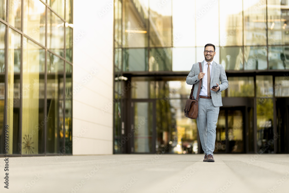 Young succesfull business man walking of the office, holding phone 