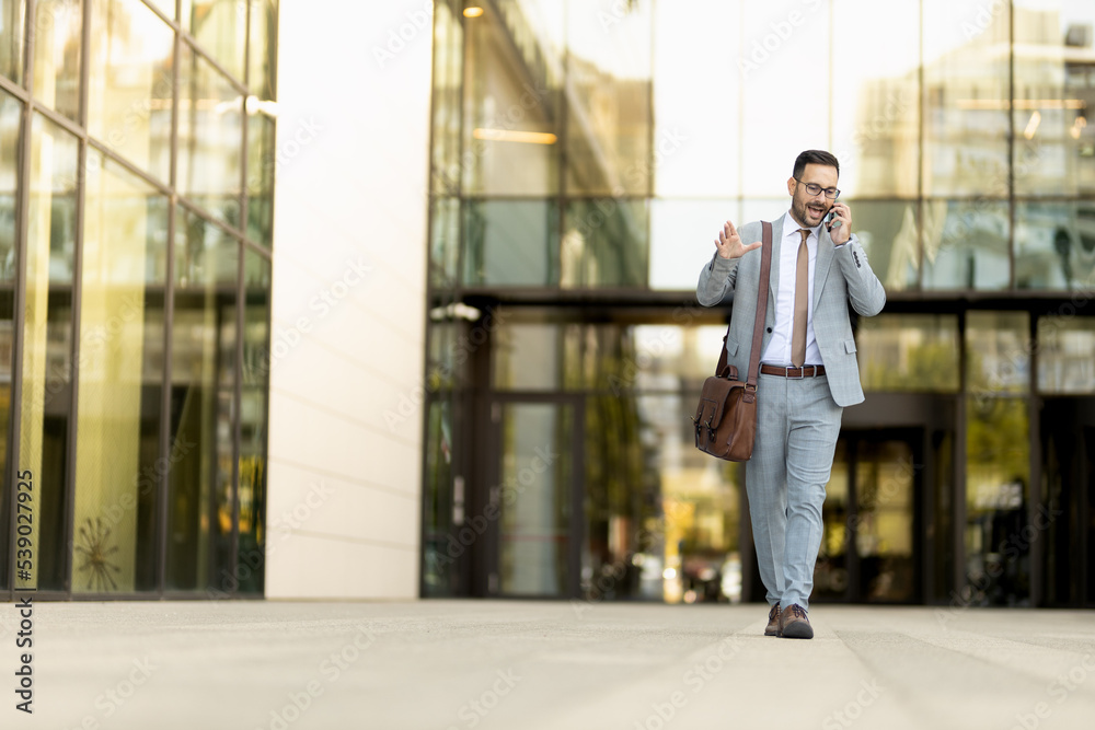 Young succesfull business man walking of the office, holding phone 