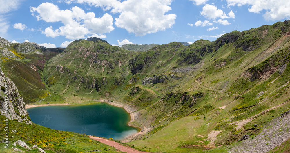 Vistas del paisaje asturiano del Lago de La Cueva por un sendero rodeado de naturaleza, montañas verdes, flores moradas cielo azul y nubes blancas en verano de 2021, España.

