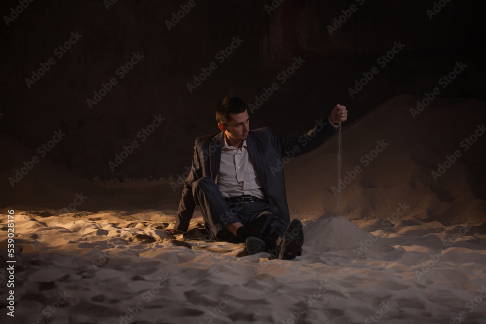 Sandbox for young businesses, startups and financial projects, concept. A young man in a business suit is playing with sand, making impossible plans Sandbox for young businesses, startups and financial projects, concept. A young man in a business suit is playing with sand, making impossible plans