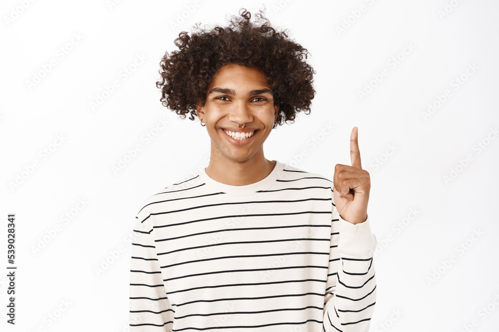 Happy smiling guy pointing finger up, showing advertisement on top, announcement or banner upwards, standing over white background Happy smiling guy pointing finger up, showing advertisement on top, announcement or banner upwards, standing over white background