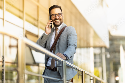 Portrait of a young business man in front of office building holding phone and looking away