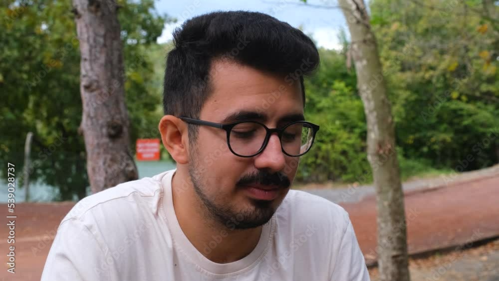 Glasses man talking and smiling, having a conversation in nature, one person Glasses man talking and smiling, having a conversation in nature, one person