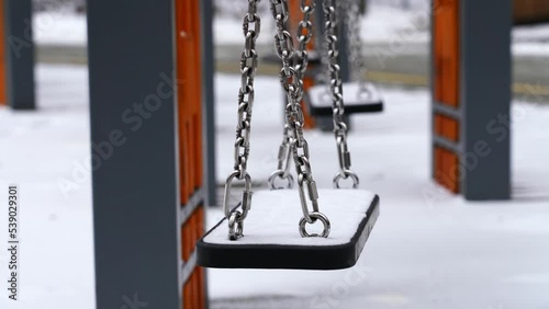 A swing covered with snow swings in the wind in winter after a snowfall. Children rocked the swing
