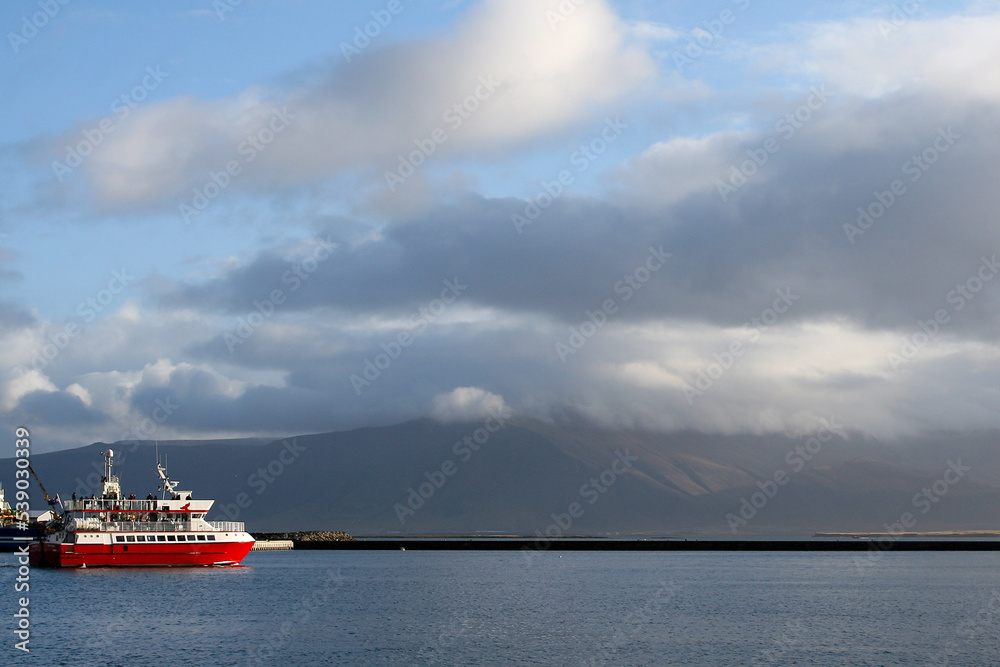 A lone red cruise ship on the water under a dramatic cloudy sky off the coast of Reykjavik, Iceland.  Image has copy space.