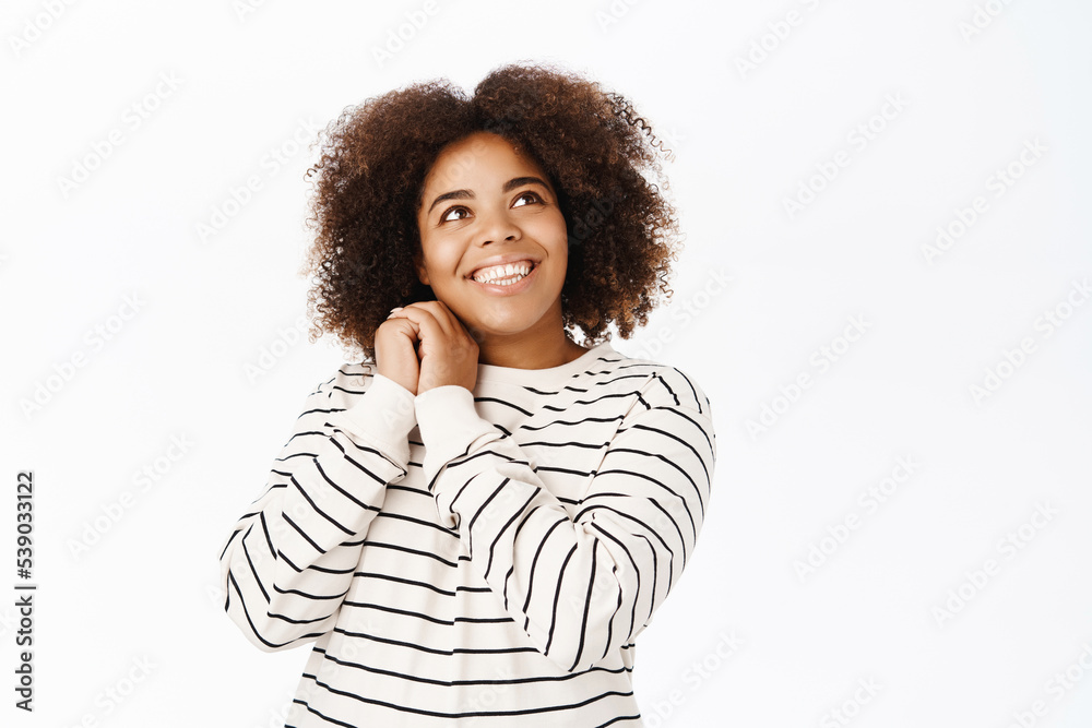 Romantic african american girl daydreaming, looking up with dreamy lovely gaze, standing over white background Romantic african american girl daydreaming, looking up with dreamy lovely gaze, standing over white background
