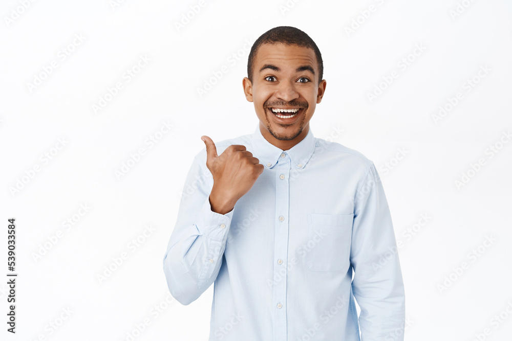 Smiling arab man pointing left, showing direction, company logo or banner aside, standing over white background in blue collar shirt Smiling arab man pointing left, showing direction, company logo or banner aside, standing over white background in blue collar shirt