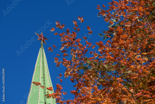 Close-up view of red star on Troitskaya Tower of Moscow Kremlin in autumn sunny day. Blurred orange rowan tree leaves in foreground. Copy space for your text. Selective focus. Travel in Russia theme. photo