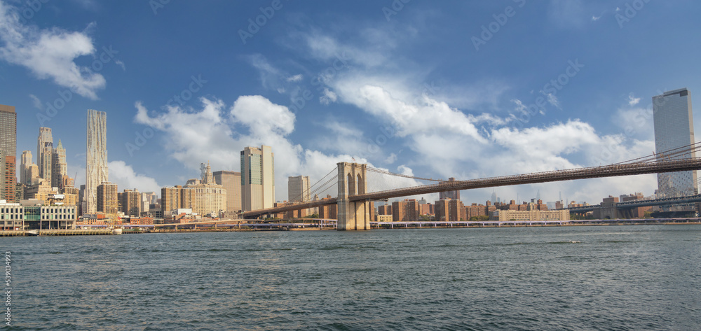 Panorama of the Brooklyn Bridge with a beautiful cloudy sky against the backdrop of the skyscrapers of Manhattan overlooking the East River Panorama of the Brooklyn Bridge with a beautiful cloudy sky against the backdrop of the skyscrapers of Manhattan overlooking the East River