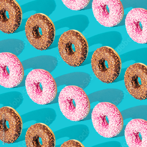 Creative pattern made of delicious chocolate and strawberry donuts on a pastel blue background. Minimal food concept.