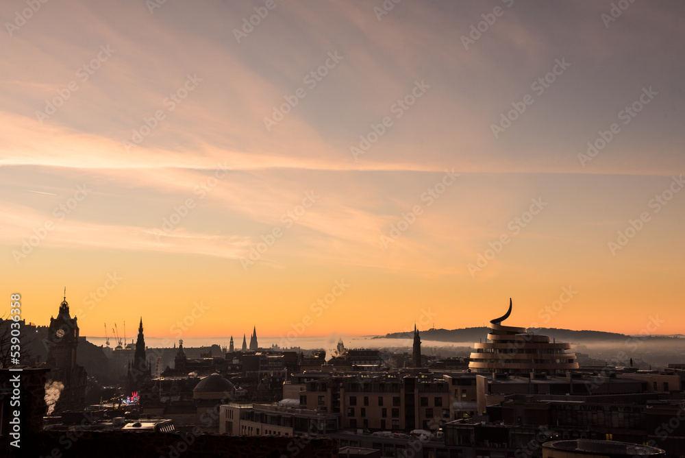 View of Edinburgh City's skyline during a misty sunset with a dramatic red sky in Scotland, United Kingdom, where famous monuments can be seen on the horizon