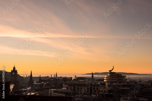 View of Edinburgh City's skyline during a misty sunset with a dramatic red sky in Scotland, United Kingdom, where famous monuments can be seen on the horizon