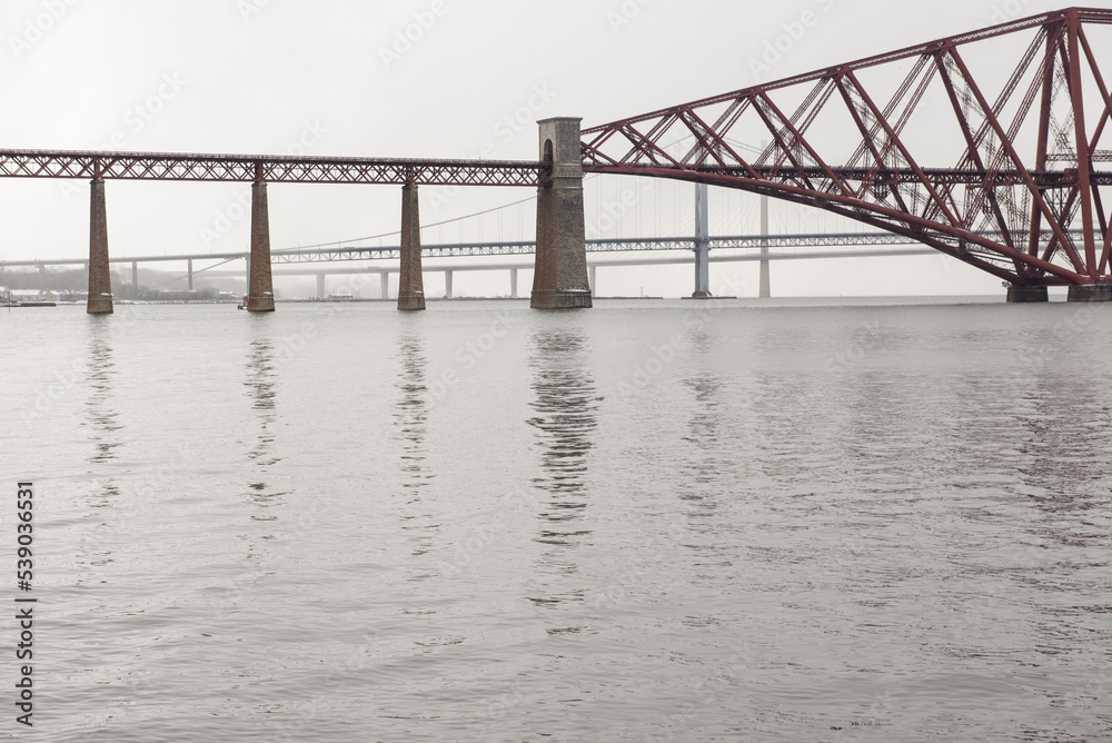 View of the George IV Bridge Rail Bridge from the distance across the Firth of Forth in an overcast Winter day in Edinburgh, Scotland, UK, with the Queensferry Crossing on the background View of the George IV Bridge Rail Bridge from the distance across the Firth of Forth in an overcast Winter day in Edinburgh, Scotland, UK, with the Queensferry Crossing on the background