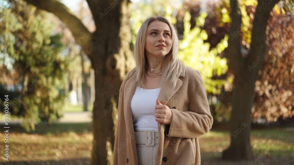 Beautiful Business Woman Walks in the Autumn City Park on a Bright Sunny Day. Attractive Blonde in a Brown Coat Walks along the Main Street of the City. Slow Motion. Beautiful Business Woman Walks in the Autumn City Park on a Bright Sunny Day. Attractive Blonde in a Brown Coat Walks along the Main Street of the City. Slow Motion.