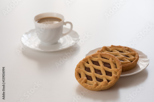 Crostate al cioccolato con tazzina bianca di caffè su tavolo bianco