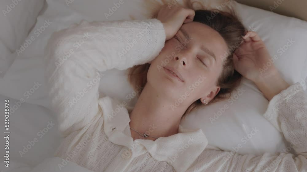 Sleepy woman waking up, turning on the pillow, smiling and stretching on the bed