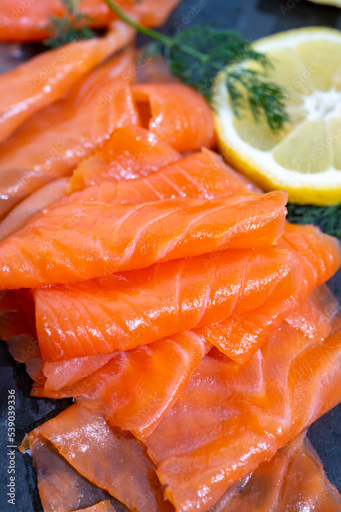 Slices of tasty smoked Scottish salmon fish served on black plate with lemon and fresh dill