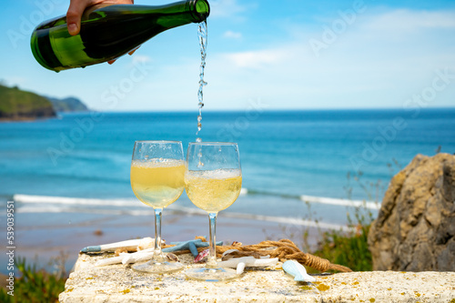 Pouring of txakoli or chacolí slightly sparkling very dry white wine produced in the Spanish Basque Country, served outdoor with view on Bay of Biscay, Atlantic Ocean. photo