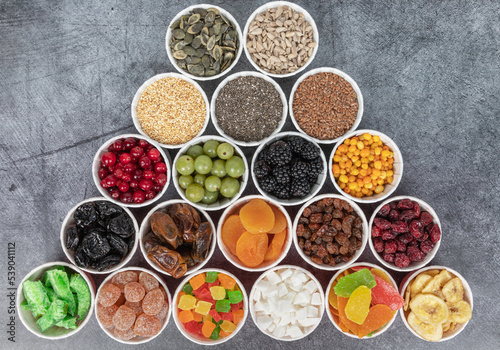 Berries, seeds, dried fruits in round containers. Background with a mix of healthy snacks. Assorted vitamin food on a grey background.