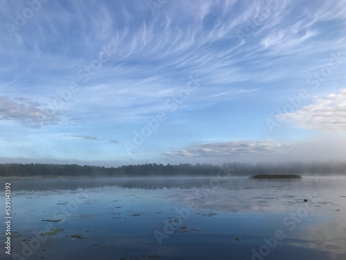 Fog over the water. Summer landscape on the lake with blue sky with reflection of clouds in the lake. Tourism and travel concept. © Elizaveta