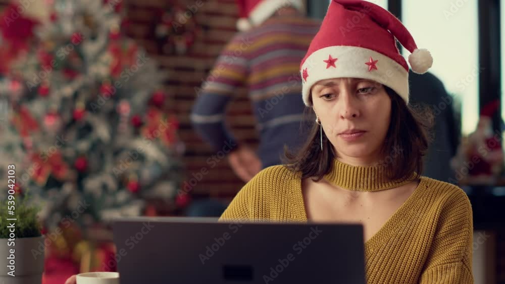 Female employee analyzing research data on laptop, wearing santa hat during christmas eve holiday season. Working on computer to plan report before celebrating winter event. Tripod shot. Female employee analyzing research data on laptop, wearing santa hat during christmas eve holiday season. Working on computer to plan report before celebrating winter event. Tripod shot.