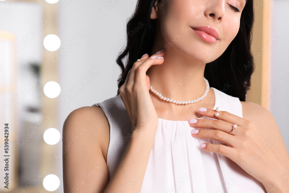 Young woman wearing elegant pearl jewelry indoors, closeup