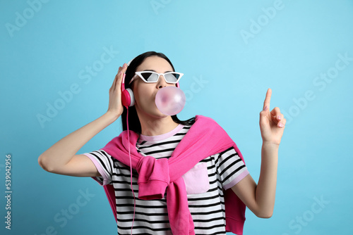 Φωτογραφία Fashionable young woman with headphones blowing bubblegum on light blue backgrou
