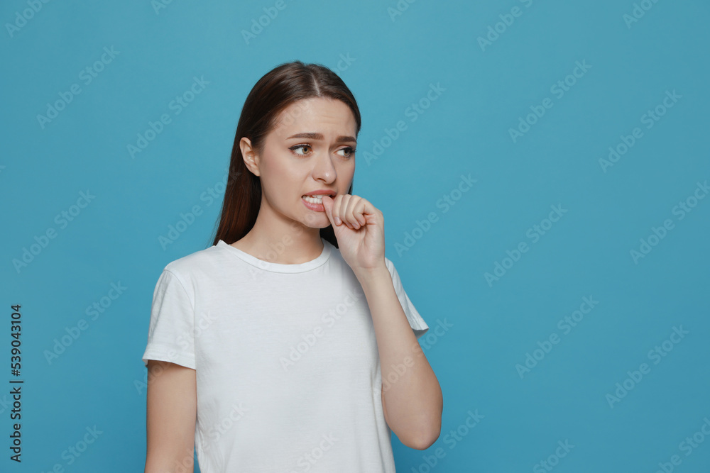 Young woman biting her nails on light blue background. Space for text Young woman biting her nails on light blue background. Space for text
