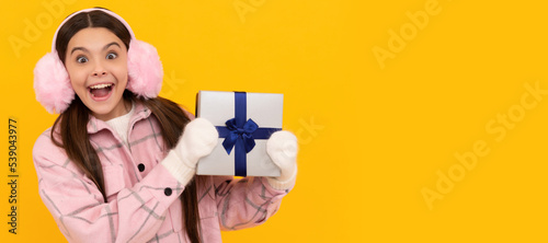 teen girl in mittens hold present on yellow background. xmas holiday gift. Banner of christmas child girl, studio kid winter portrait with copy space.