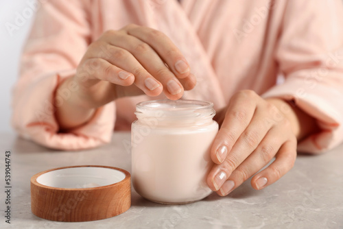 Woman applying hand cream at grey table, closeup