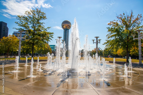 a gorgeous autumn landscape at World's Fair Park with a water fountain surrounded by autumn colored trees, lush green trees and the Sunsphere with blue sky and clouds in Knoxville Tennessee USA photo