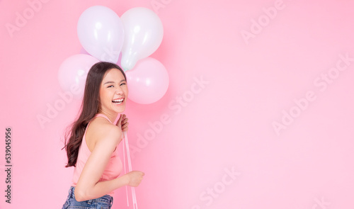 Excited cheerful asian woman holding balloons and hands beside mouth smiling with toothy standing over isolated pink background. Joyful teenager girl with pastel balloons shocked  amazed expression.