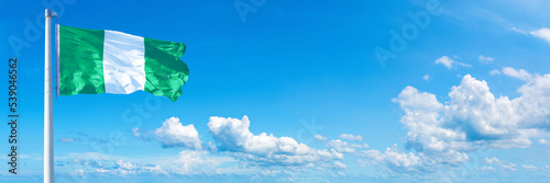 Nigeria flag waving on a blue sky in beautiful clouds - Horizontal banner
