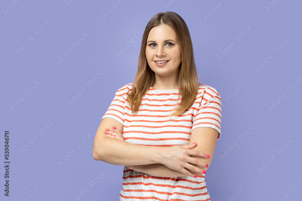 Portrait of cheerful joyful blond woman wearing striped T-shirt standing with folded hands, being in good mood, expressing happiness. Indoor studio shot isolated on purple background. Portrait of cheerful joyful blond woman wearing striped T-shirt standing with folded hands, being in good mood, expressing happiness. Indoor studio shot isolated on purple background.