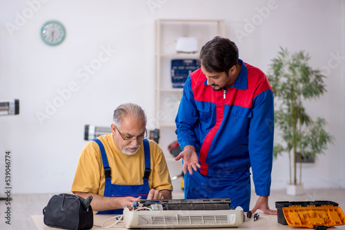 Two male repairmen repairing air-conditioner